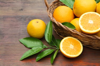 Photo of Wicker basket, ripe juicy oranges and green leaves on wooden table