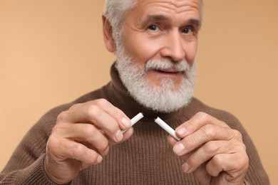 Photo of Stop smoking concept. Senior man holding pieces of broken cigarette on beige background, selective focus