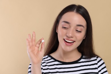 Photo of Happy woman showing pill on beige background