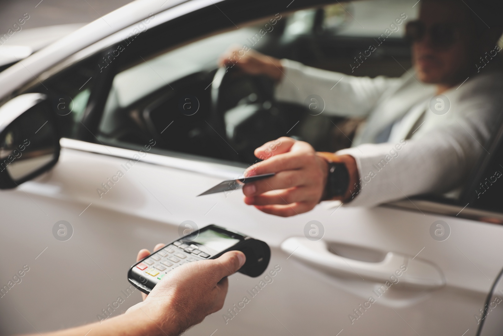 Photo of Man sitting in car and paying with credit card at gas station, focus on hand