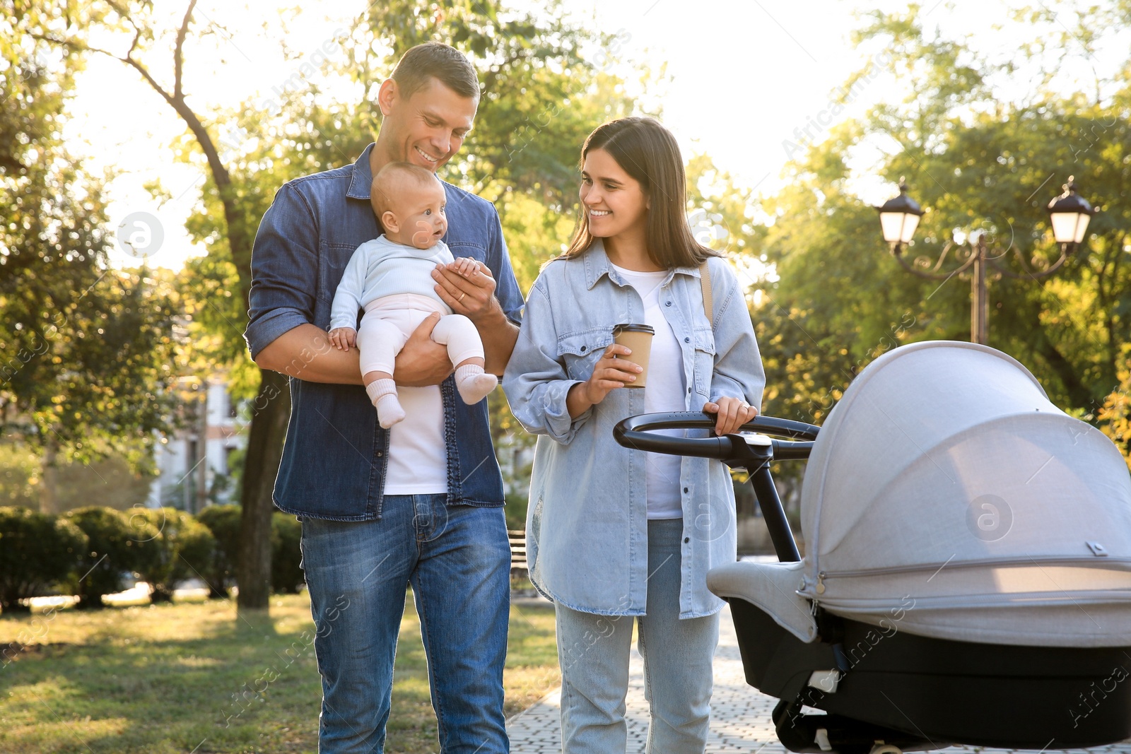 Photo of Happy parents walking with their baby in park on sunny day