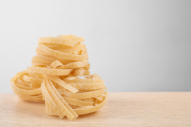 Uncooked tagliatelle pasta on wooden table against grey background. Space for text