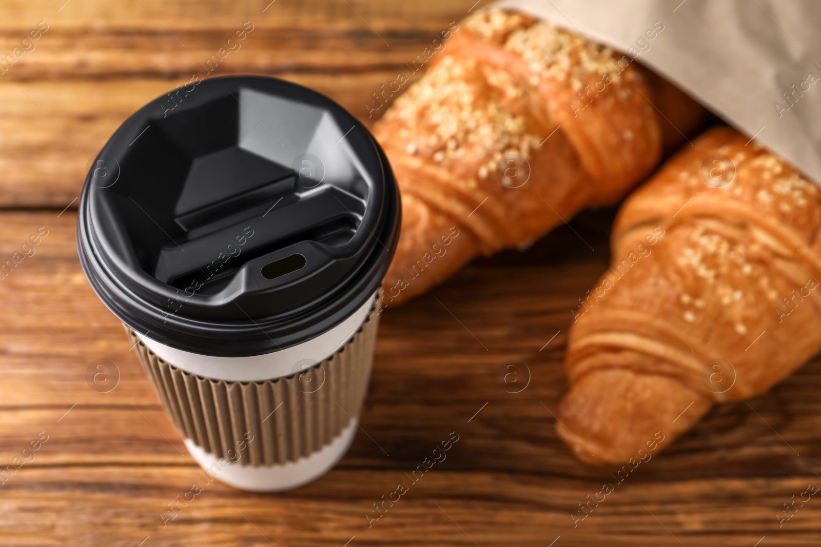 Photo of Coffee to go. Paper cup with tasty drink and pastry on wooden table, closeup