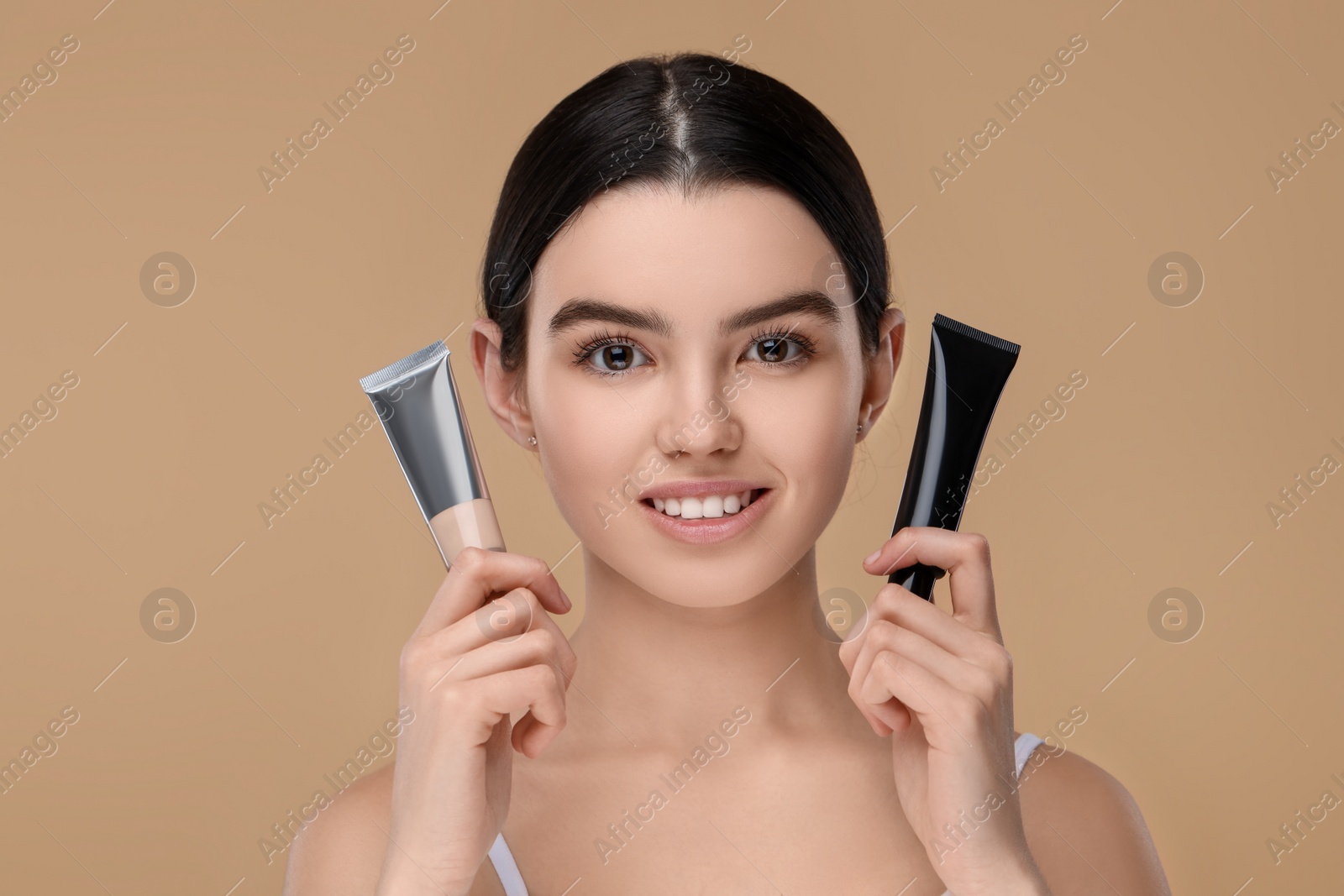 Photo of Teenage girl holding tubes with foundation on beige background