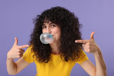 Beautiful young woman blowing bubble gum on purple background