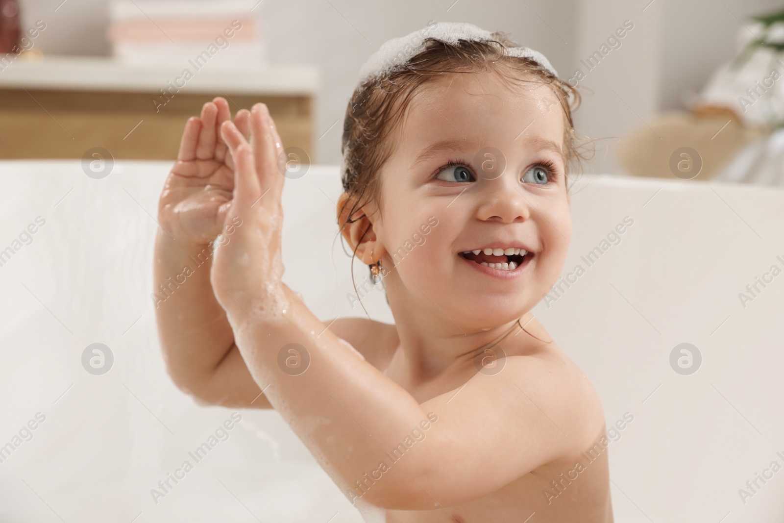 Photo of Cute little girl washing hair with shampoo in bathroom