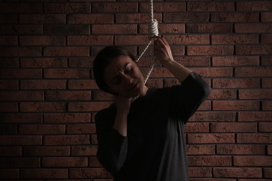 Depressed woman with rope noose on neck near brick wall