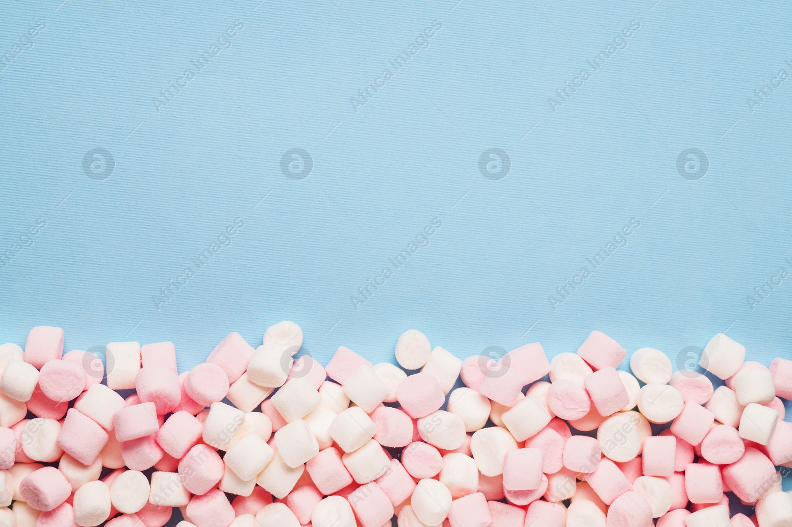 Photo of Delicious marshmallows on light blue background, flat lay. Space for text