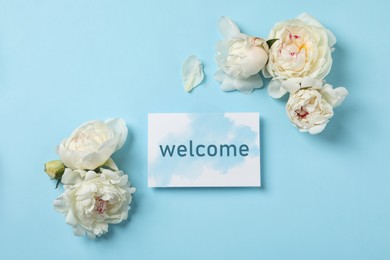 Fresh peonies and card with word WELCOME on light blue background, flat lay