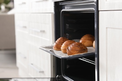 Photo of Open oven with tray of freshly baked buns in kitchen