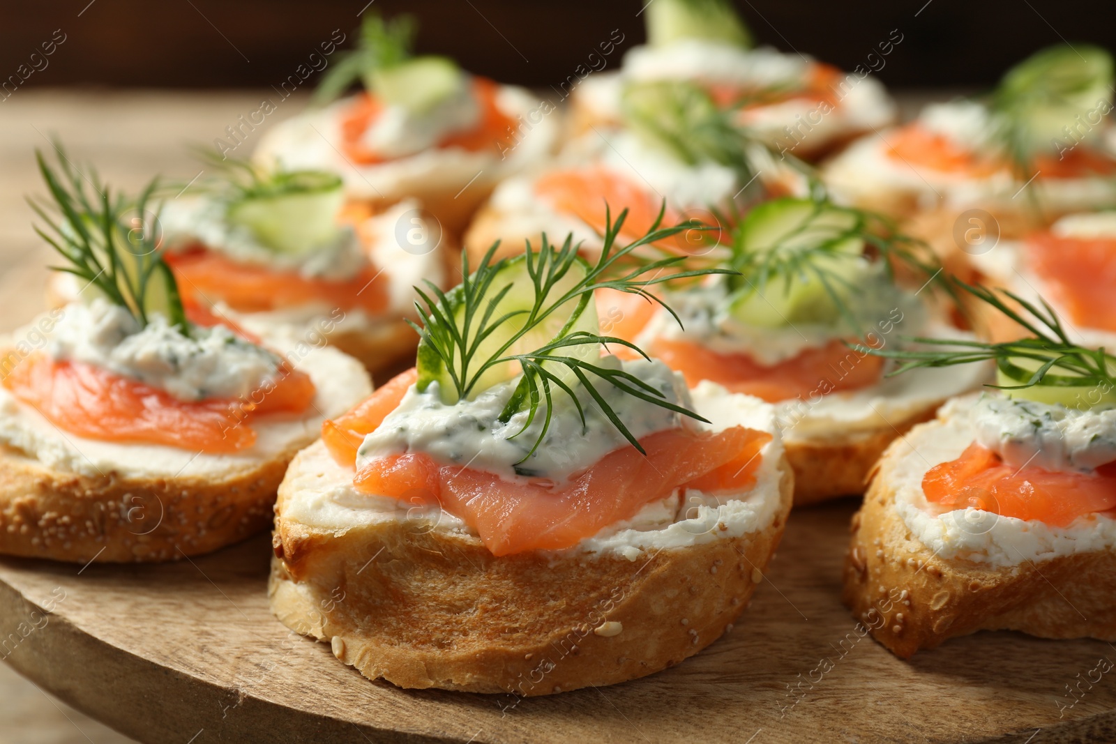 Photo of Tasty canapes with salmon, cucumber, cream cheese and dill on wooden stand, closeup