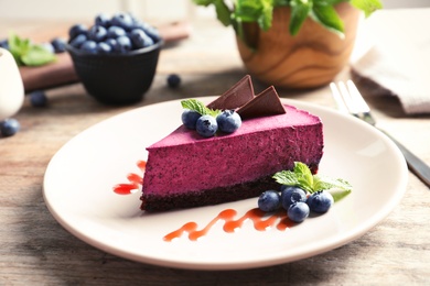 Photo of Plate with piece of tasty blueberry cake on wooden table