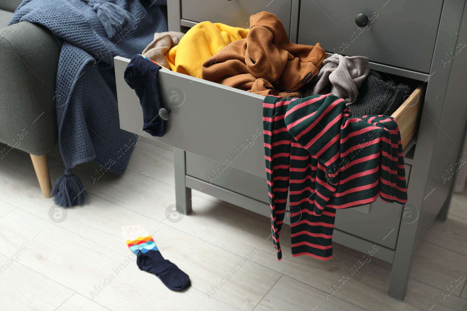 Photo of Cluttered chest of drawers indoors. Clothes in mess