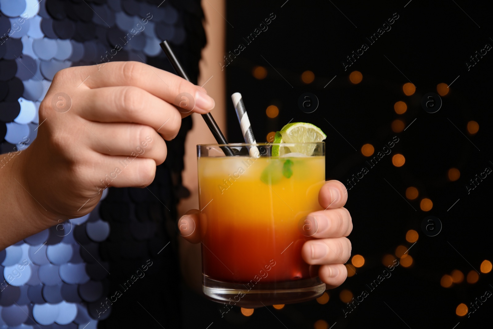 Photo of Woman with glass of Tequila Sunrise on blurred background, closeup. Delicious alcoholic cocktail