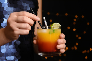 Woman with glass of Tequila Sunrise on blurred background, closeup. Delicious alcoholic cocktail