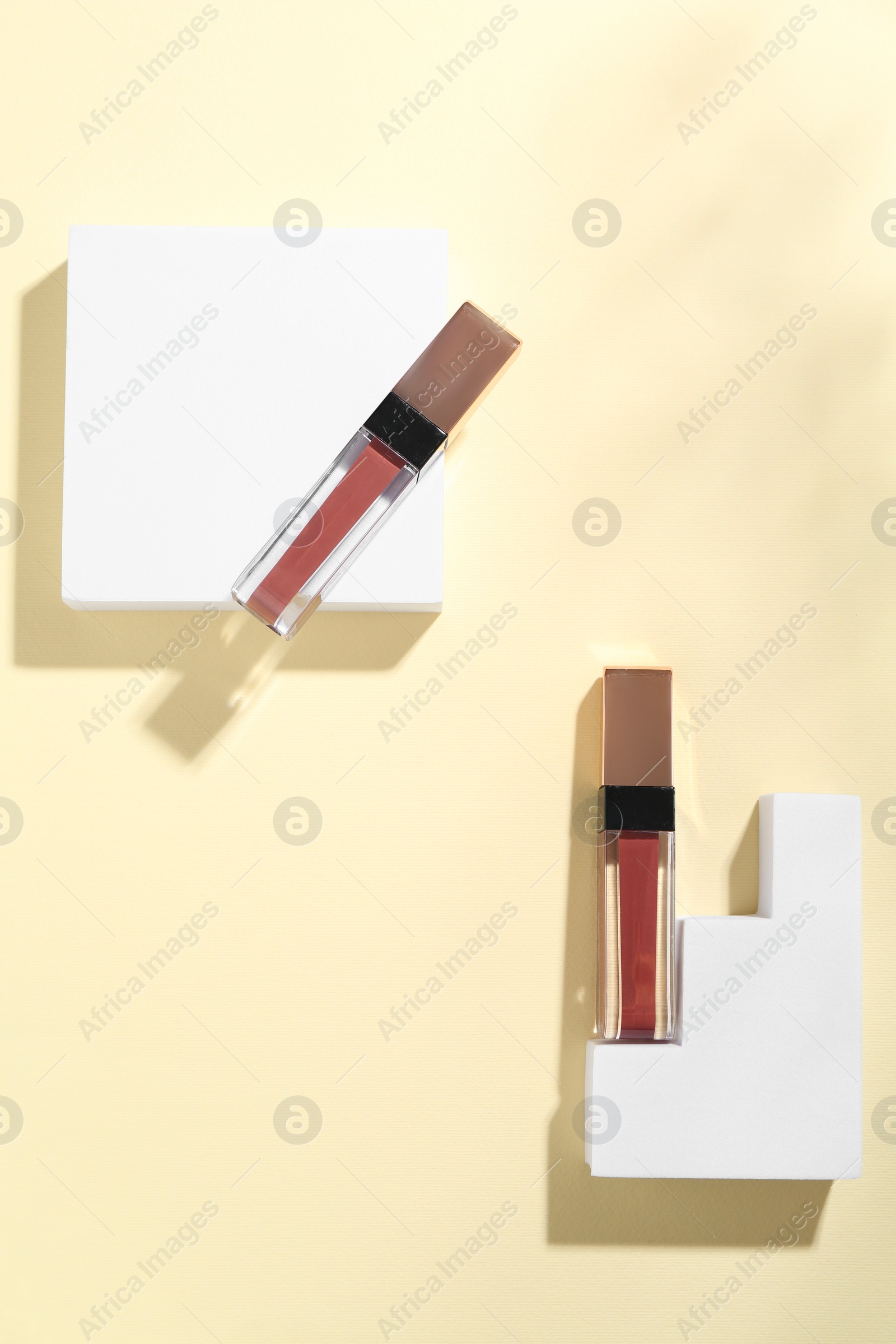 Photo of Lip glosses and podiums on pale yellow background, top view