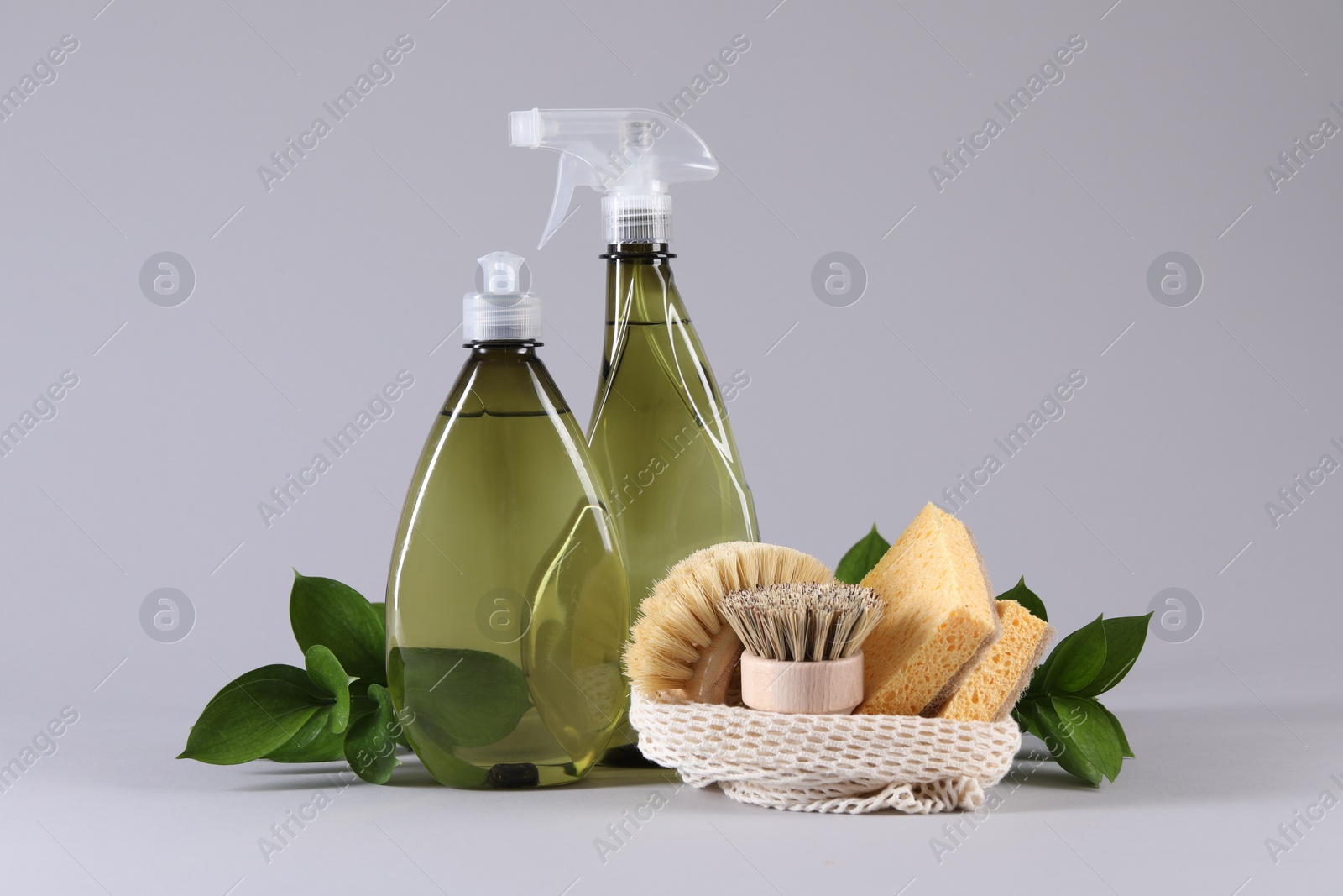 Photo of Bottles of cleaning product, sponges, brushes and floral decor on light background