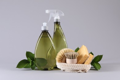 Photo of Bottles of cleaning product, sponges, brushes and floral decor on light background