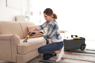 Photo of Woman removing dirt from sofa with vacuum cleaner at home