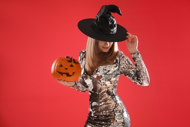 Photo of Beautiful woman in witch costume with jack o'lantern on red background. Halloween party