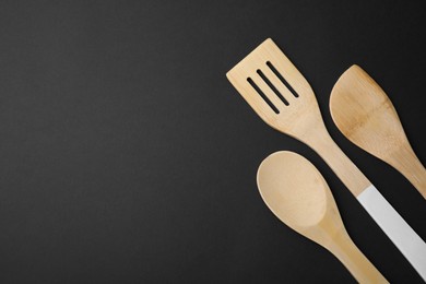 Wooden kitchen utensils on black background, flat lay. Space for text