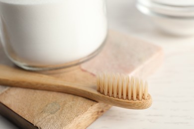Bamboo toothbrush and jar of baking soda on white table, closeup