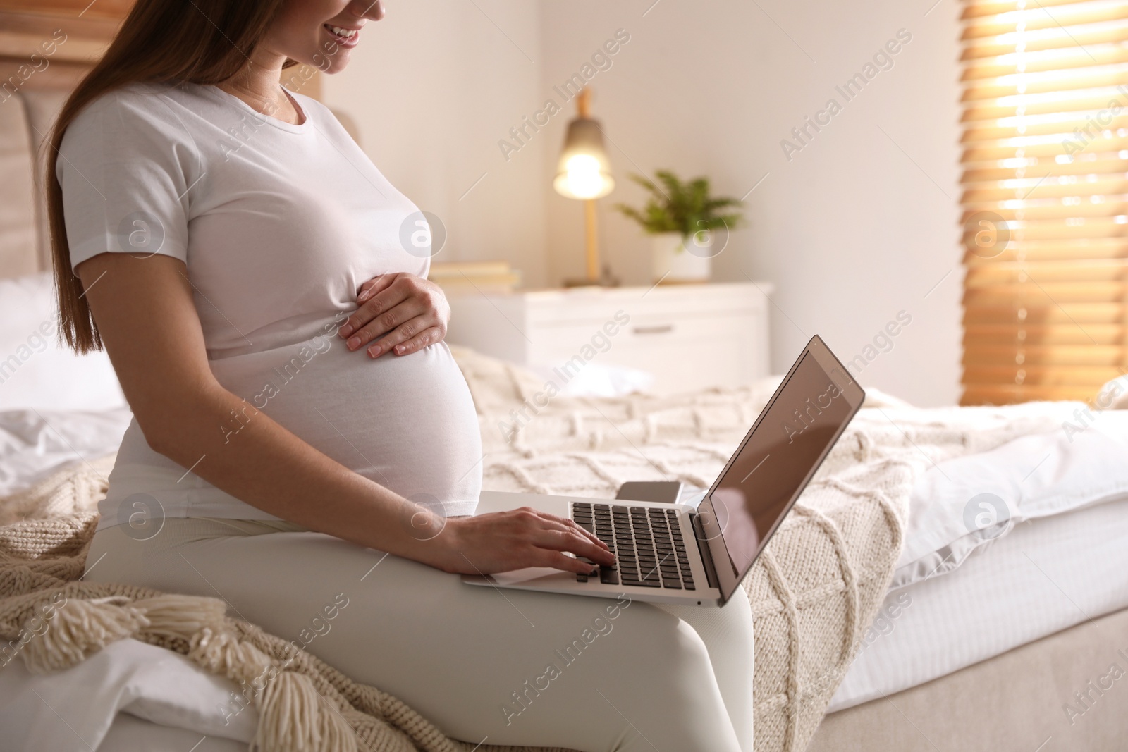 Photo of Pregnant woman working on bed at home, closeup. Maternity leave