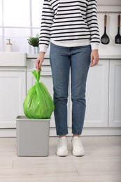 Photo of Woman taking garbage bag out of trash bin in kitchen, closeup