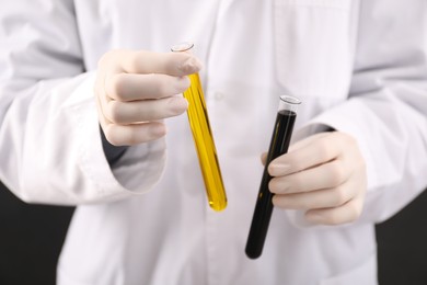 Photo of Woman holding test tubes with different types of crude oil on dark background, closeup