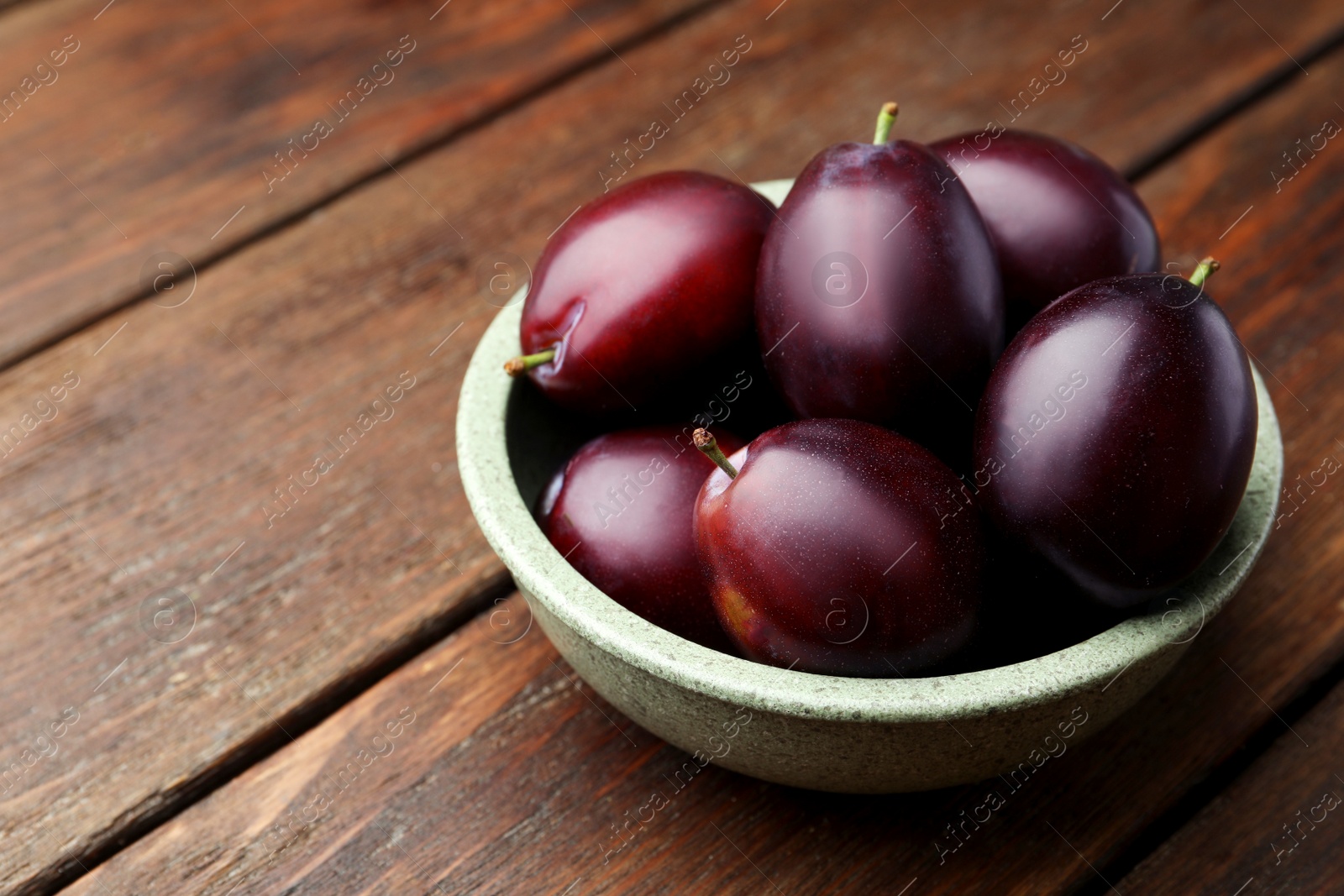 Photo of Tasty ripe plums in bowl on wooden table