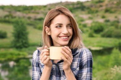 Young woman with drink in metal mug outdoors. Camping season