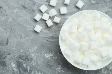 Photo of White sugar cubes in bowl on grey table, top view. Space for text