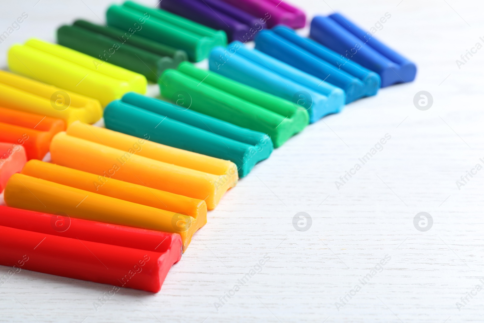 Photo of Many different colorful plasticine on white wooden table, closeup. Space for text