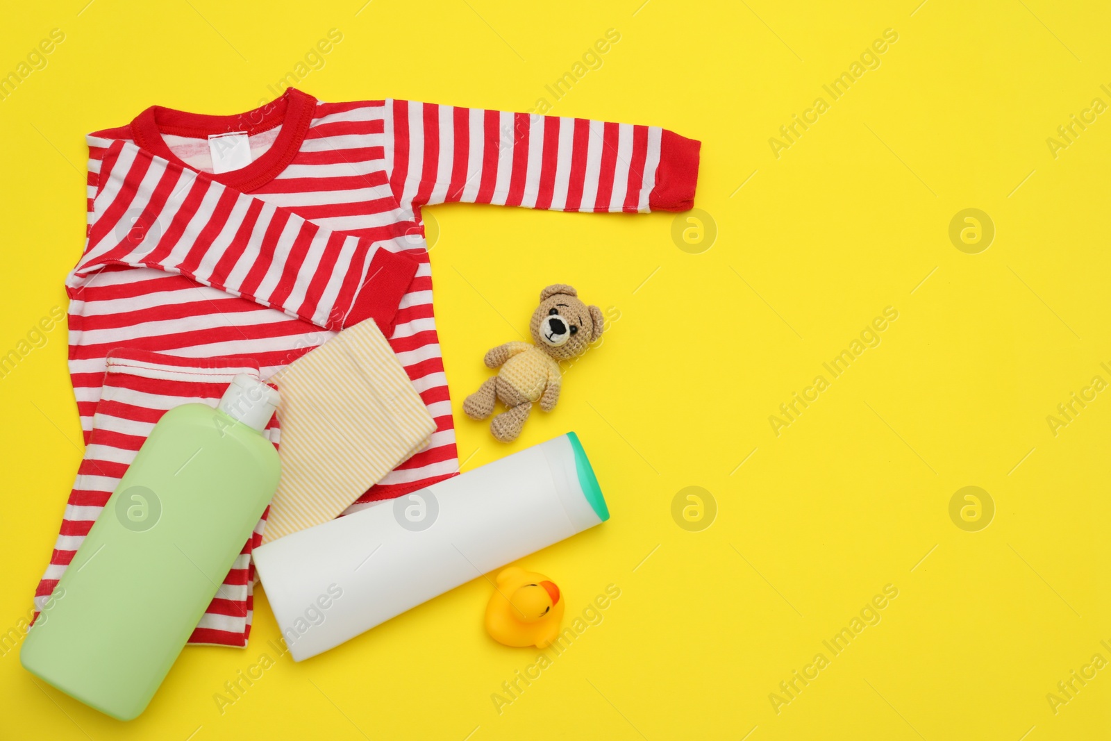 Photo of Bottles of laundry detergents, baby clothes and toy bear on yellow background, flat lay. Space for text