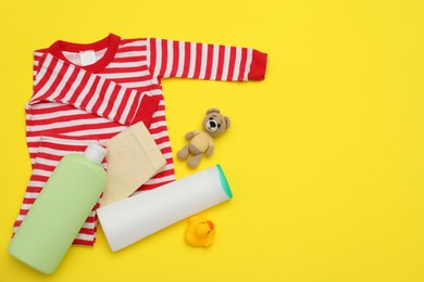 Bottles of laundry detergents, baby clothes and toy bear on yellow background, flat lay. Space for text