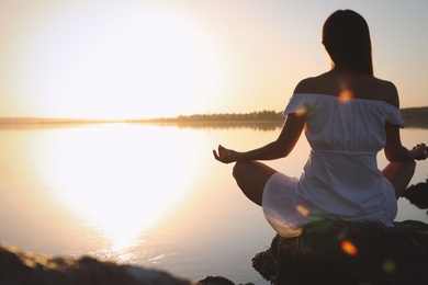 Woman practicing yoga near river on sunset. Healing concept