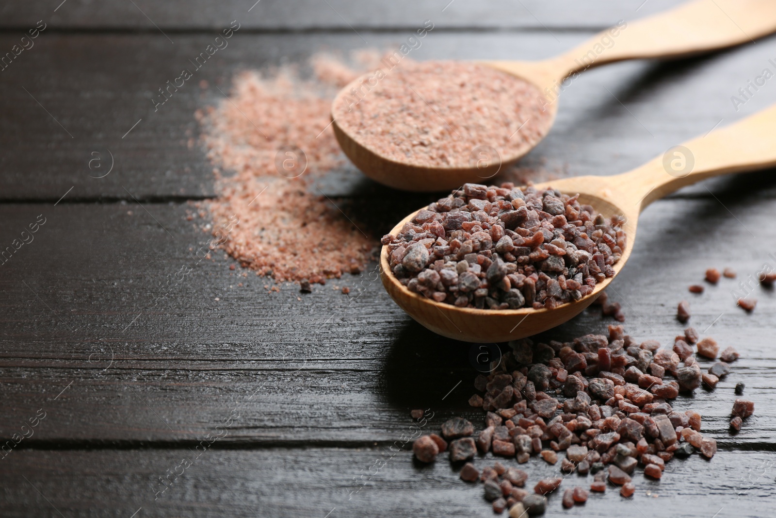 Photo of Spoons with black salt on wooden table, closeup