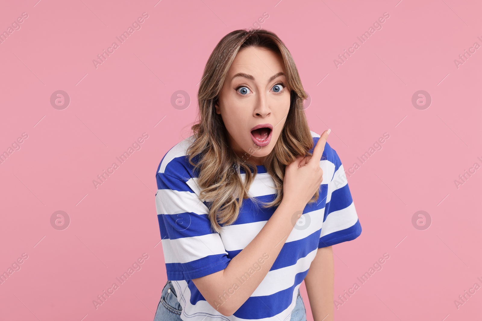 Photo of Portrait of surprised woman pointing at something on pink background