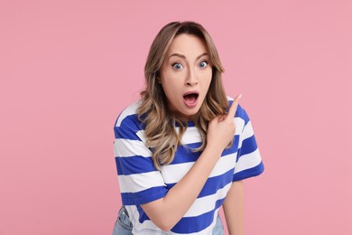 Portrait of surprised woman pointing at something on pink background