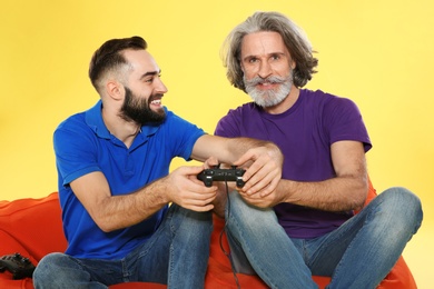 Mature man and guy playing video games with controllers on color background