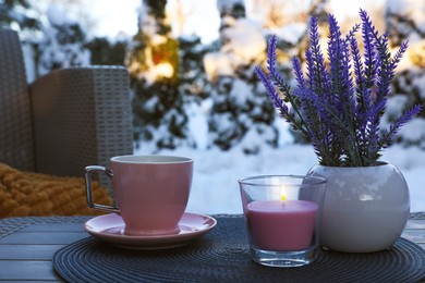 Burning candle, potted flowers and cup of hot drink on coffee table outdoors. Cosy winter