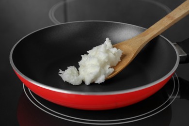 Photo of Frying pan with coconut oil and spatula on induction stove, closeup. Healthy cooking