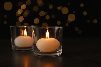 Photo of Burning candles in glass holders on table against blurred lights