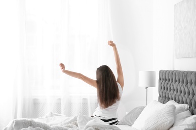 Photo of Young beautiful woman stretching after sleeping on bed at home