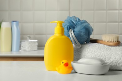 Baby cosmetic products, bath duck, brush and towel on white table. Space for text