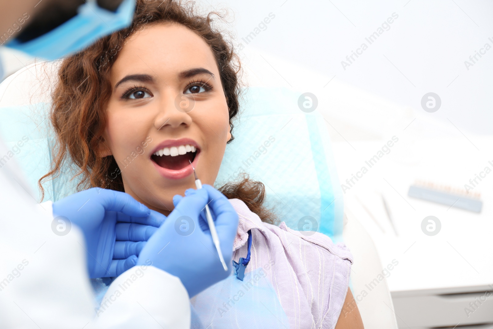 Photo of Dentist examining African-American woman's teeth with probe in hospital. Space for text