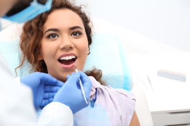 Dentist examining African-American woman's teeth with probe in hospital. Space for text