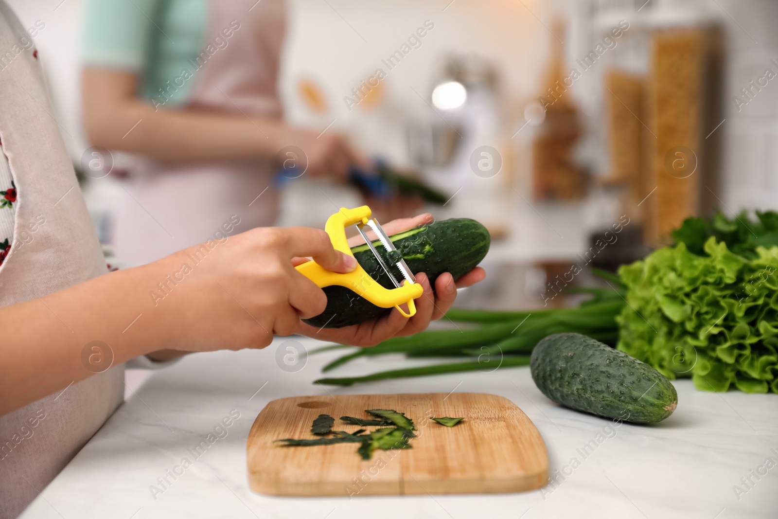 Photo of Mother and daughter peeling vegetables at kitchen counter, closeup