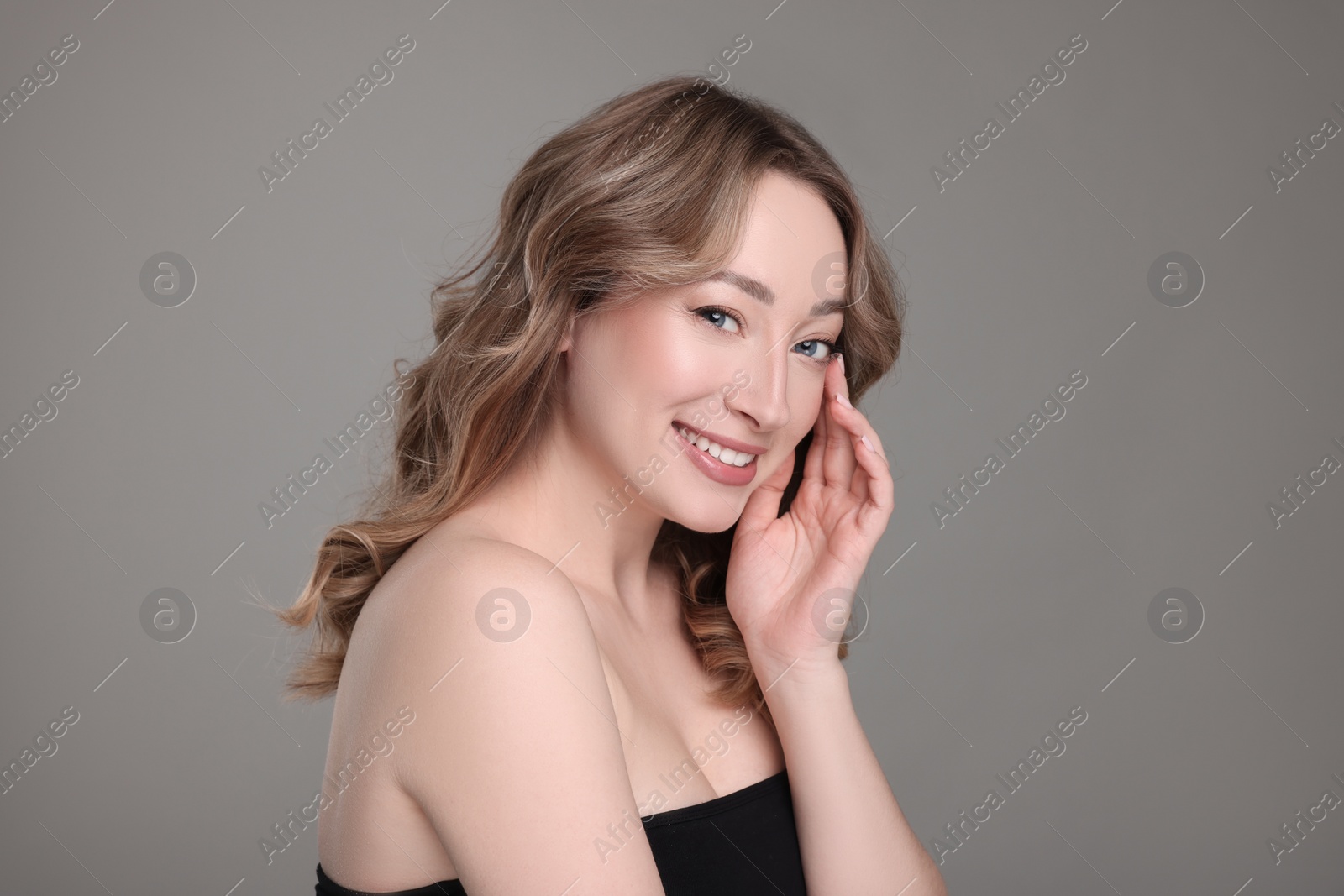 Photo of Portrait of smiling woman with curly hair on grey background