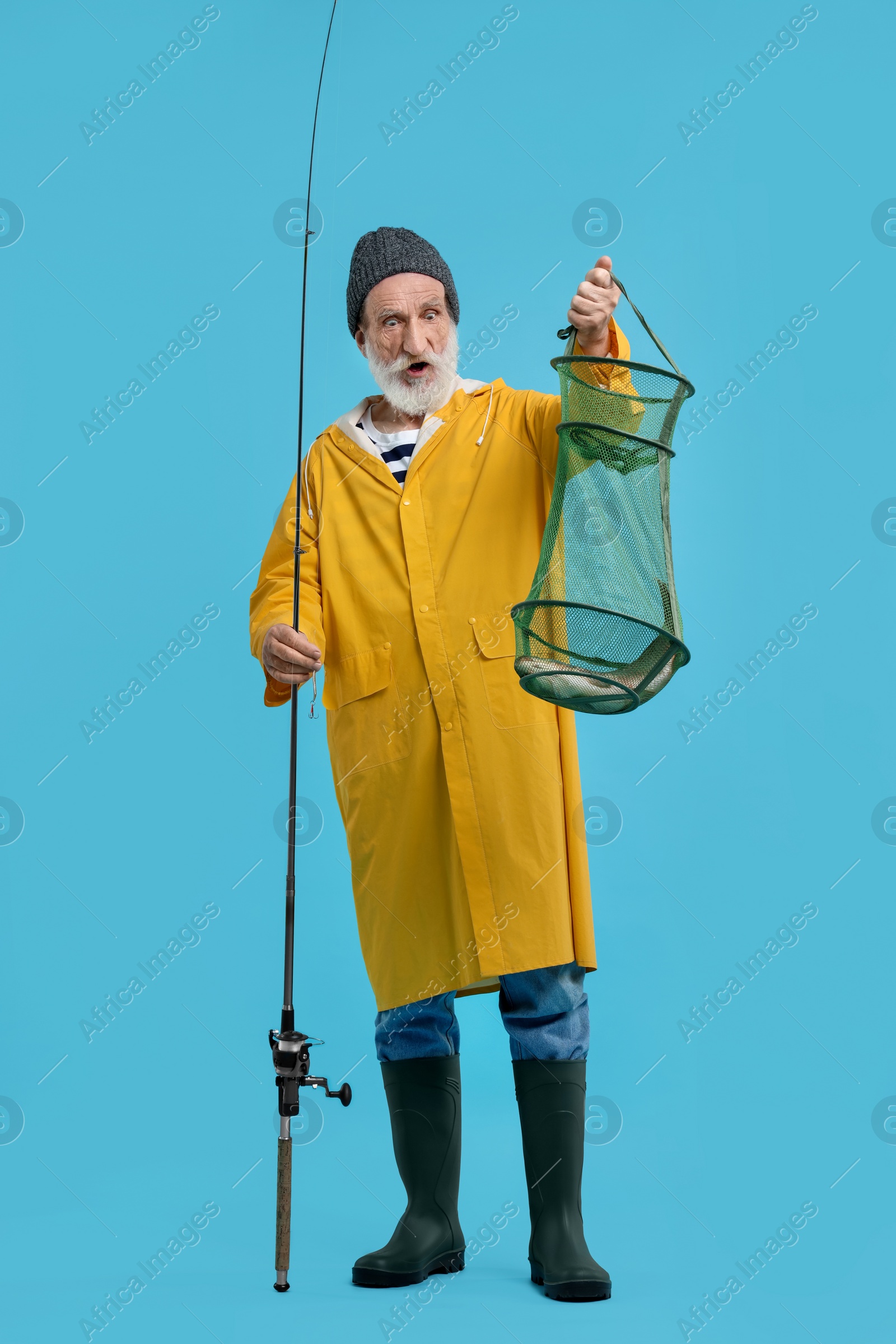 Photo of Fisherman holding rod and fishing net with catch on light blue background